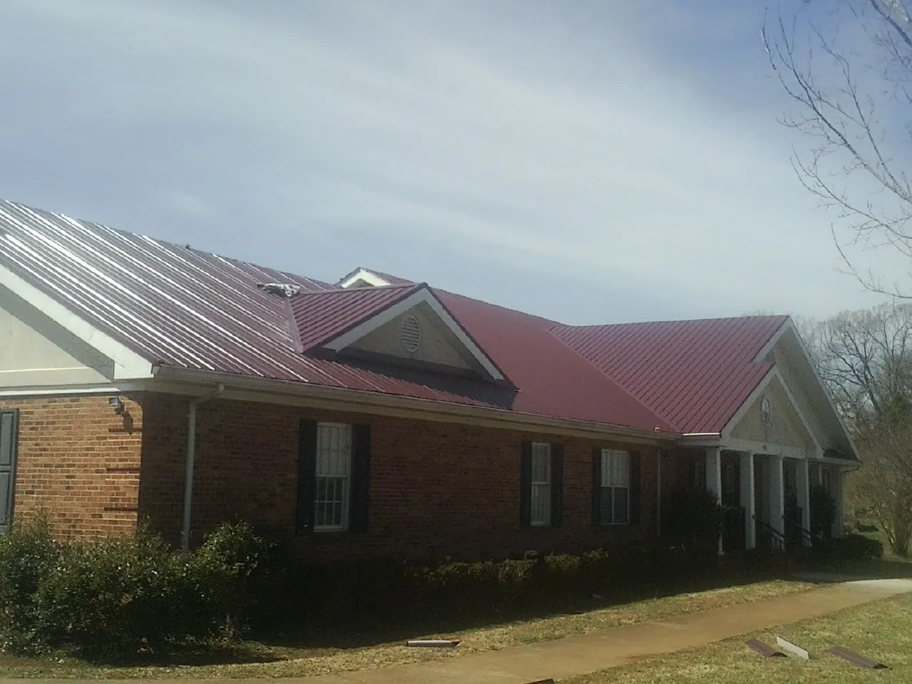 Red metal roof with gabled entries on a long brick building, from a Hail Damage Roof Repair job in Sleepy Eye