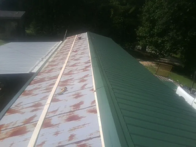 Old rusted panels beside newly installed green metal roofing — Wind Damage Roof Repair by Roofing Brothers in Sleepy Eye