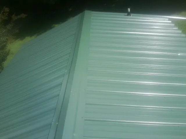 New green metal panels meeting at the ridge of a roof — Flat Roof Repair work by our crew in Sleepy Eye