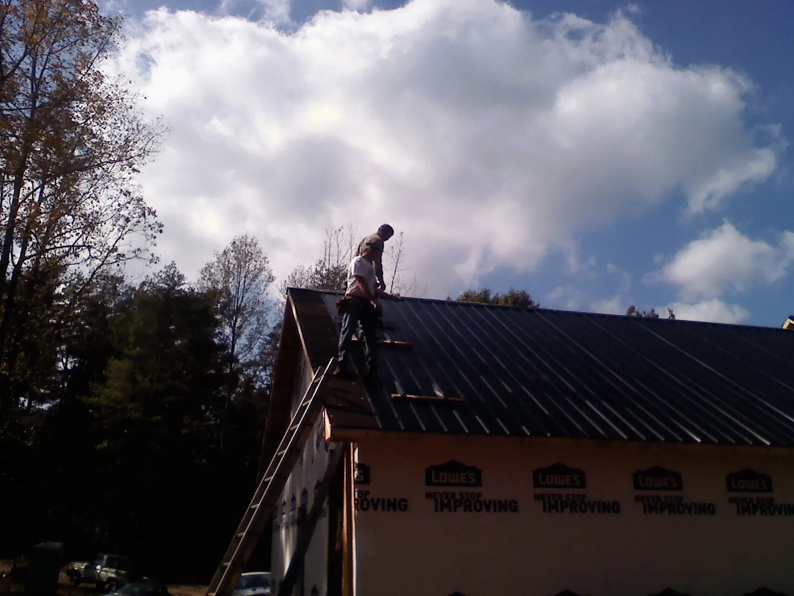Roofer fastening dark metal panels high against a cloudy sky, from a Roof Inspection job in Sleepy Eye