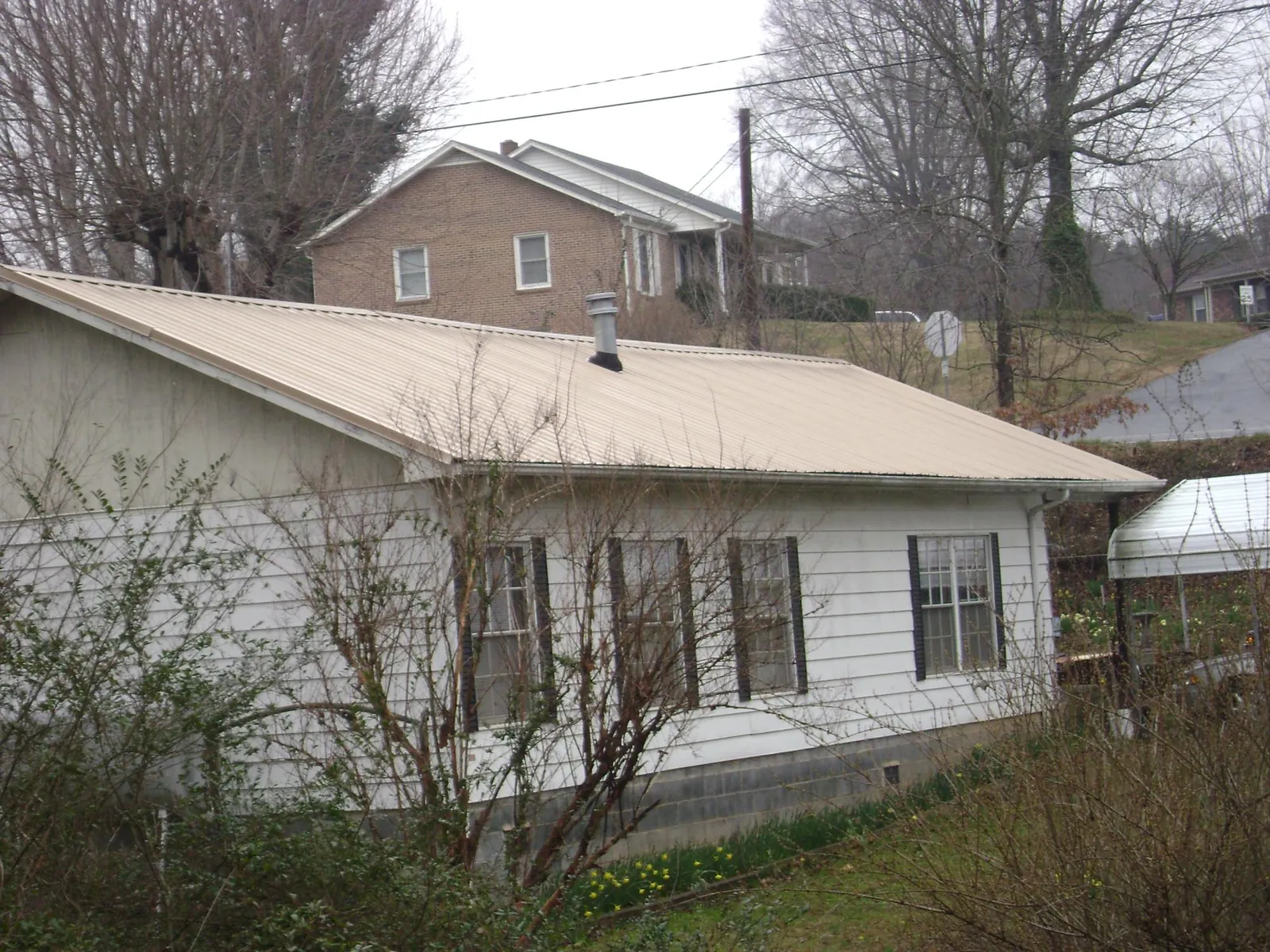 Tan metal roof on a white sided house set into a hillside — Commercial Roofing by Roofing Brothers in Sleepy Eye