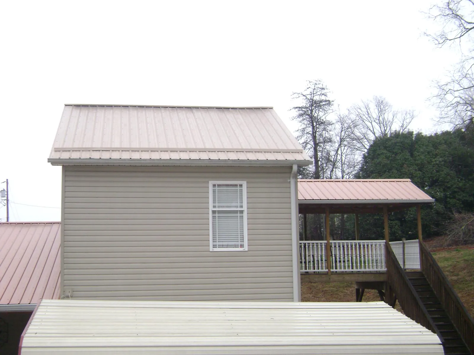 Tan metal roofs on a two story addition and attached porch, from a Roof Replacement job in Sleepy Eye